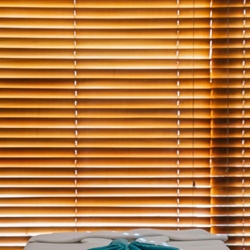 pexels-photo-6560312-6560312 A serene spa setting featuring a massage table with teal towel and wooden window blinds.
